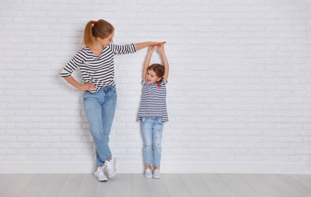concept of the family. mother measures growth of child to daughter near empty wall - tall human height women measuring imagens e fotografias de stock