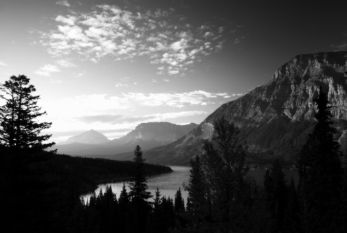 A black and white photograph featuring an idyllic landscape featuring a lake with rock formations appearing from the fog