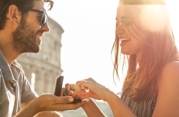 feliz pareja joven en propuesta de matrimonio de amor con anillo sentado en el bar delante de coliseo de roma al atardecer. destello de lente - lens box fotografías e imágenes de stock