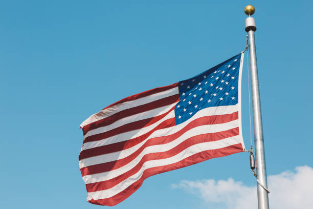 istock Low Angle View Of American Flag Fluttering Against Blue Sky 910880962