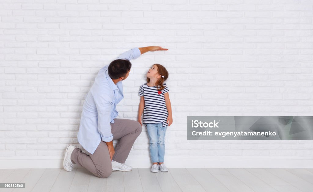 concept of the family. the father measures growth of child to daughter near empty wall concept of the family. the father measures growth of child to a daughter near an empty wall Child Stock Photo