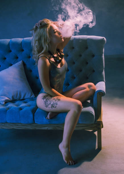 istock sexy young woman on sofa vaping e-cigarette against dark blue background 910885980