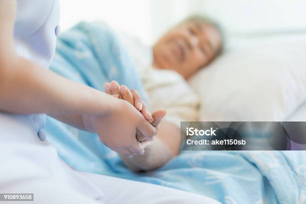 Nurse Sitting On A Hospital Bed Next To An Older Woman Helping Hands Care For The Elderly Concept Stock Photo - Download Image Now