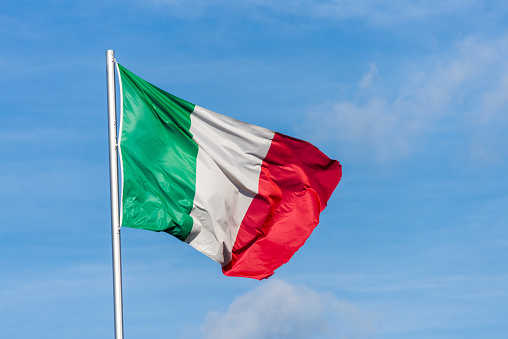 Closeup of single italian tricolor flag waving in the wind in front of blue sky