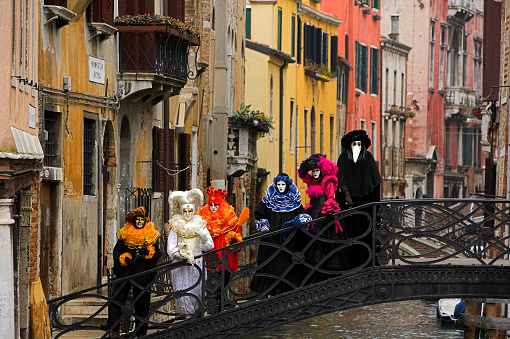 Venice, Italy - March 01, 2022: Couple dressed in traditional costumes stand in front of the Bridge of Sighs, part of the Venice Mask Carnival, Veneto, Italy