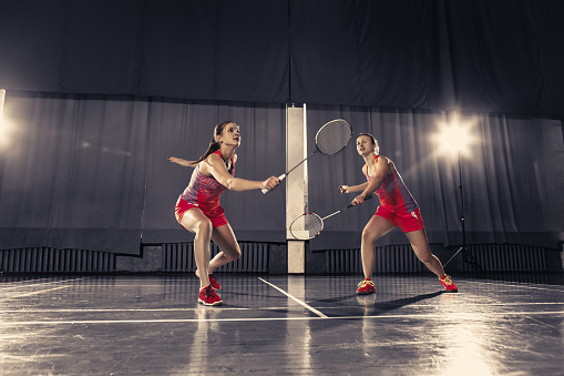 The two young women playing badminton over gym background. concept game in a pair