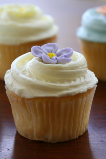 Cute trio of vanilla cupcakes with frosting and flowers.