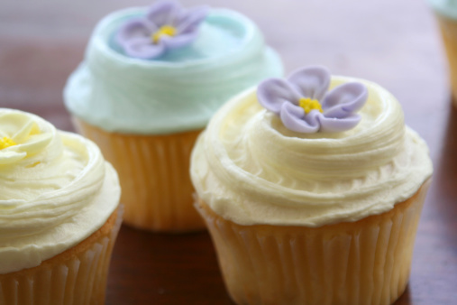 Cute trio of vanilla cupcakes with frosting and flowers.