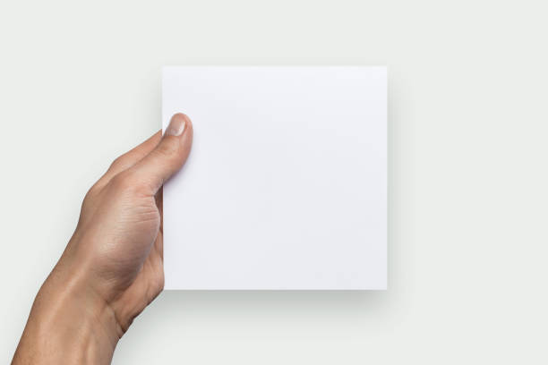 istock Mockup square empty blank white postcard holds the man in his hand. Isolated on a gray background 910987002