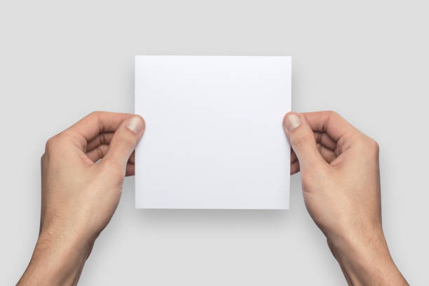 istock Mockup square empty blank white postcard holds the man in his hand. Isolated on a gray background 910987022