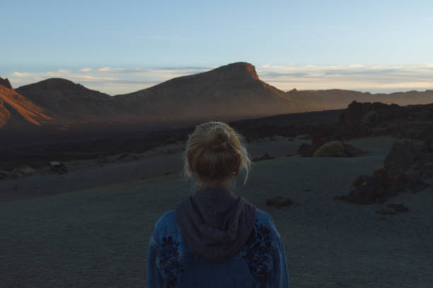 istock Young girl from behind in desert looking at mountains during sunset 910995676