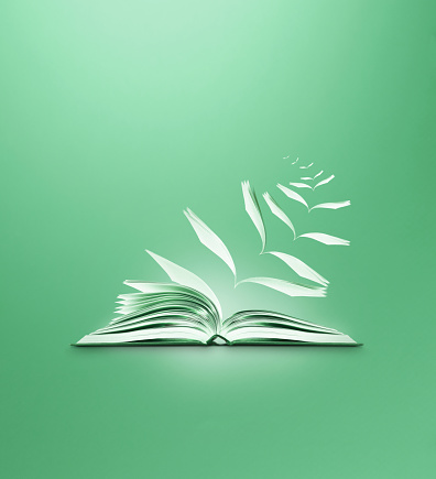 Conceptual image of an open book with pages flying away with a green background and copy space. The image suggests the power of imagination and magical, inspirational freedom and escape offered by storytelling and reading