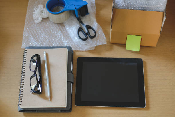 istock notebook, tablet, packing accessories at workplace of startup small business owner. cardboard parcel box for online selling. entrepreneur, SME seller desk. e-commerce, shipping concept 911008070