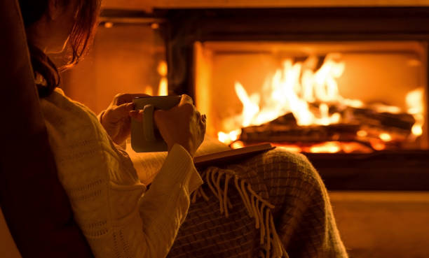 Young woman sitting at home by the fireplace and reading a book. stock photo