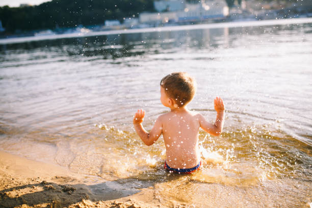 istock boy child playing makes splashes, beats hands on the water in the river at sunset 911018420