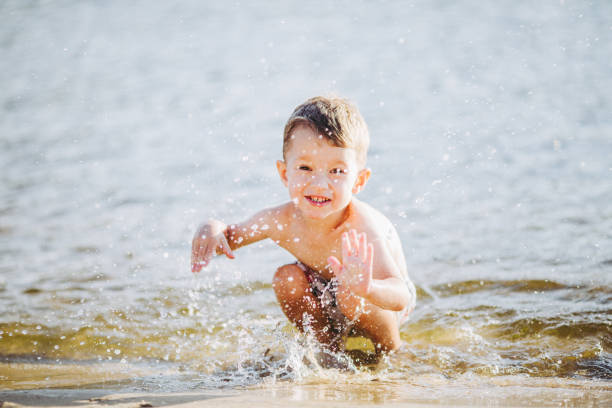 istock boy child playing makes splashes, beats hands on the water in the river at sunset 911018698