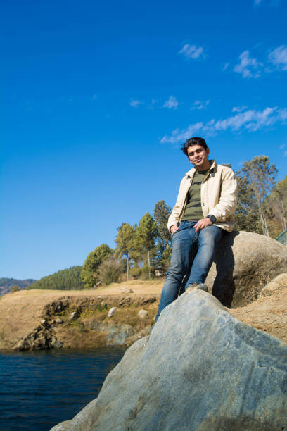 istock Young man sitting on stone at hill lake 911021696