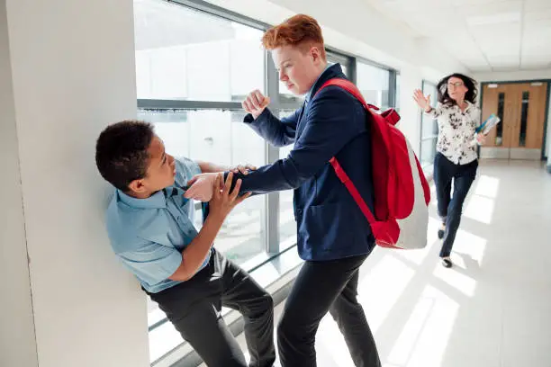 Redhead teenage male bullying mixed race teenage boy in the corridor at school.