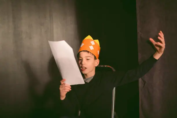 11 years old boy enjoying drama club rehearsal. Holding script and reading.