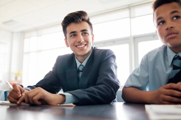Smiling Student Low angle view of mixed race male student smiling sat at desk. school boy in uniform stock pictures, royalty-free photos & images