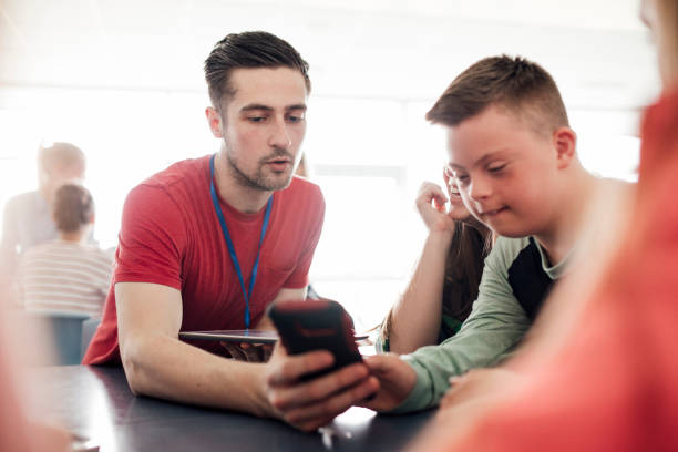 Support for Students Point of view angle of teacher assisting down syndrome boy with using the smart phone. down syndrome photos stock pictures, royalty-free photos & images