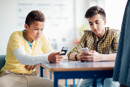 Teenage male students using their phones in class.