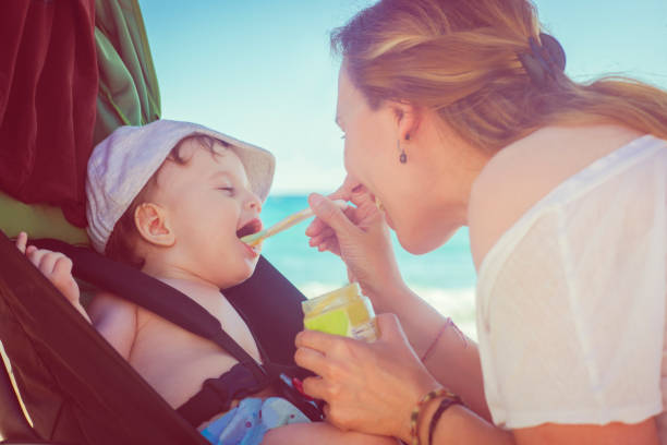 istock Happy mother feeding her baby boy on the beach 911034430