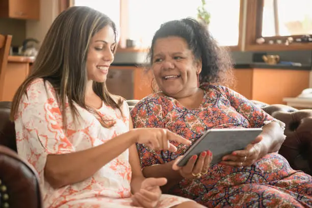 Aboriginal young woman showing her mother how to use tablet, pointing at the screen