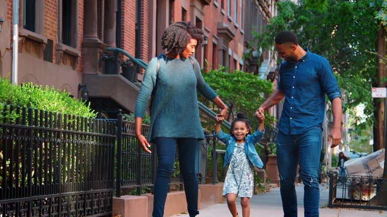 Young black couple swinging daughter as they walk in the street