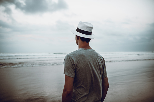 Rear View of Lonely Man with Hat Looking at Stormy Ocean