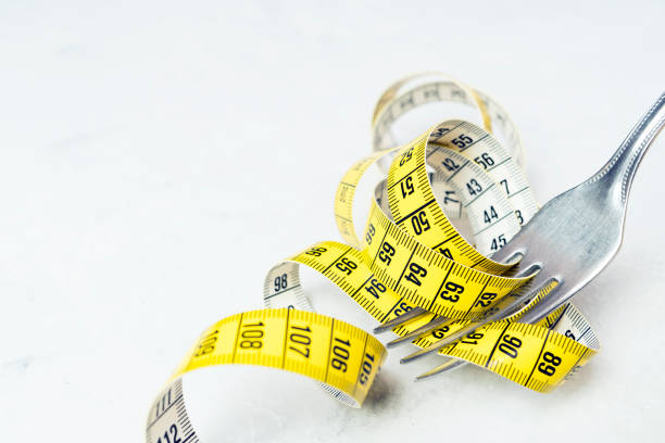 istock The measuring tape is yellow, wrapped around a fork lying on a white surface. 911113206