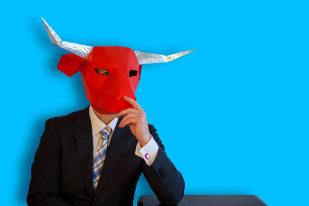 istock buisinessman with a bull mask sitting with blue background 911119224
