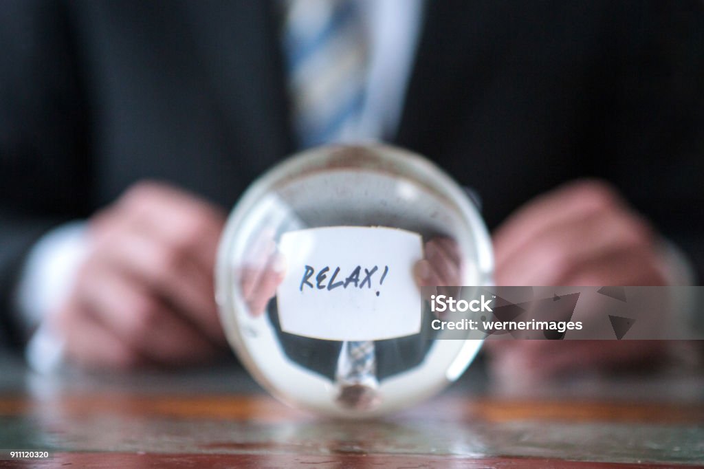 man holding paper with the word Relax in front of glass ball closeup of man holding paper with the word Relax in front of glass ball Adult Stock Photo