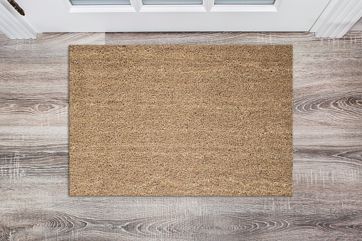 Blank tan colored coir doormat before the white door in the hall. Mat on wooden floor, product Mockup.