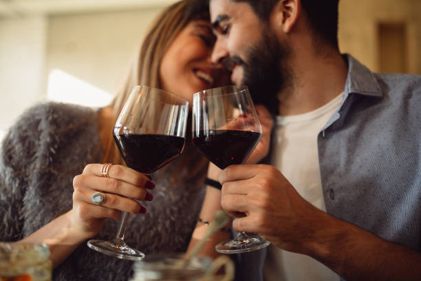 Couple clink glasses with red wine at date in casual outfit in cafe. Couple having romantic moments. stock photo