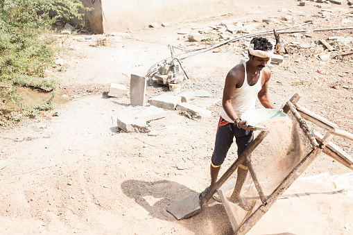 Indian man working at local village job site.  The manual laborer sifts sand for the building floor outside the construction project he is working on.  Rural villages, real life people of Southern India.