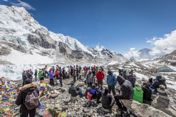 large group of tourists standing at Mount Everest base camp in sunshine A large group of tourists congregate at the edge of Mount Everest basecamp where they stop for photographs, before returning, on a sunny cold day, with a mountainous landscape all around base camp stock pictures, royalty-free photos & images