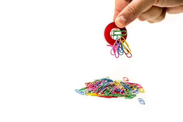 Photo of man hand holding magnet attracting metal paper clips
