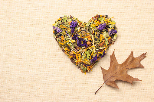 Dried herb leaves heart shaped on burlap surface. Herbaceous dry aromatic plant. Healing herbs herbal medicine concept.