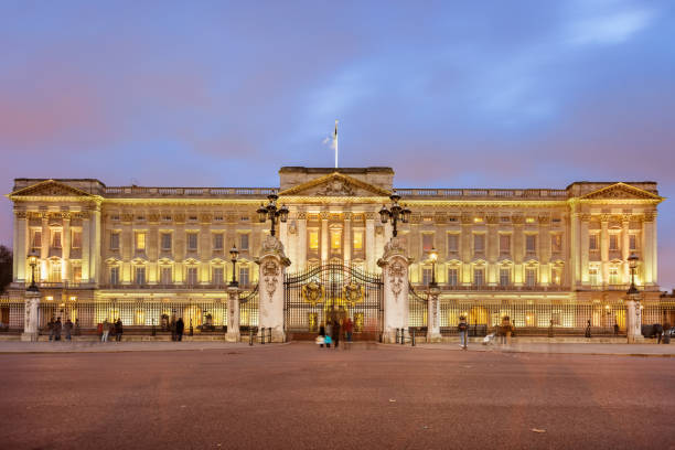 Tourists look at the landmark Buckingham Palace in Westminster, London, UK at twilight.