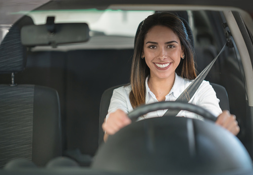 Portrait of a happy woman driving a car at garage and looking at the camera smiling - lifestyle concepts