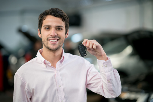 Portrait of a happy man at a garage holding keys to his car and looking at the camera smiling - vehicle breakdown concepts