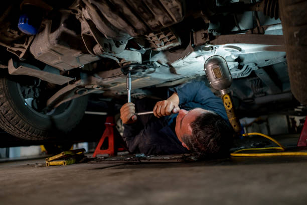 Mechanic fixing a car at an auto repair shop Mechanic fixing a car and working underneath the chassis of a vehicle at an auto repair shop mechanic working under car stock pictures, royalty-free photos & images
