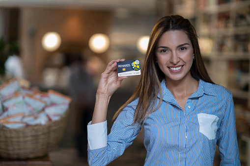 Portrait of a female customer at a grocery shop holding a rewards card and looking at the camera smiling - **DESIGN ON CREDIT CARD WAS MADE FROM SCRATCH BY US**