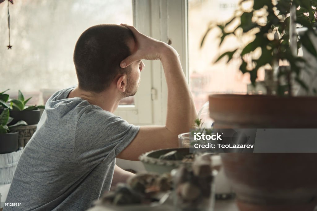 Young handsome man feeling depressed and sad Young handsome man sitting at his home, feeling lonely and depressed, beating himself up Loneliness Stock Photo