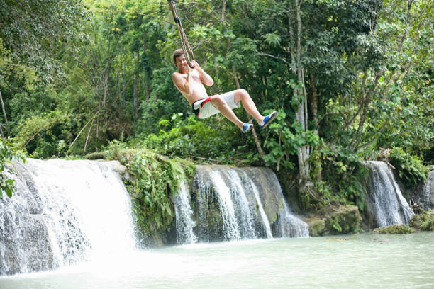 Swinging out terrified at the Cambugahay Falls on Siquijor Island, the Philippines Young male backpacker enjoys the thrill of a rope swing over a river siquijor stock pictures, royalty-free photos & images