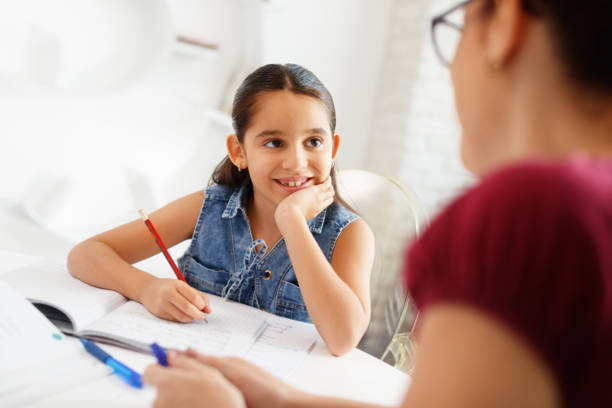 ヒスパニックの母助ける女の子やって学校の宿題を自宅 - 個人レッスン ストックフォトと画像