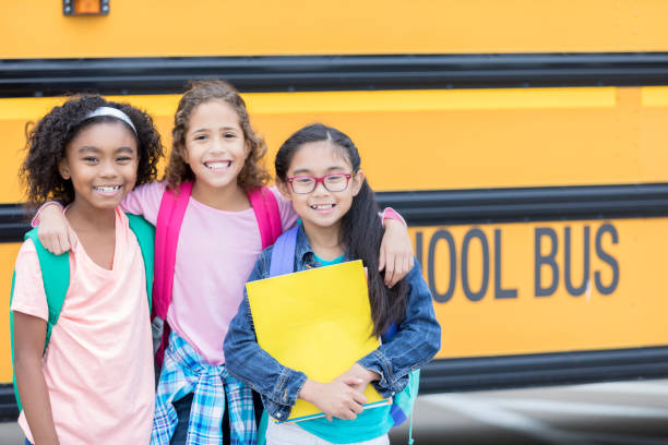 istock Elementary age female friends in front of school bus 911249942