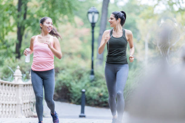 istock Two women power walk together at park 911250038