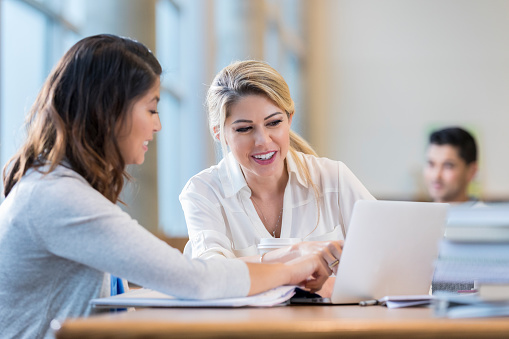 Diverse female college students review something on a laptop while studying for an exam.